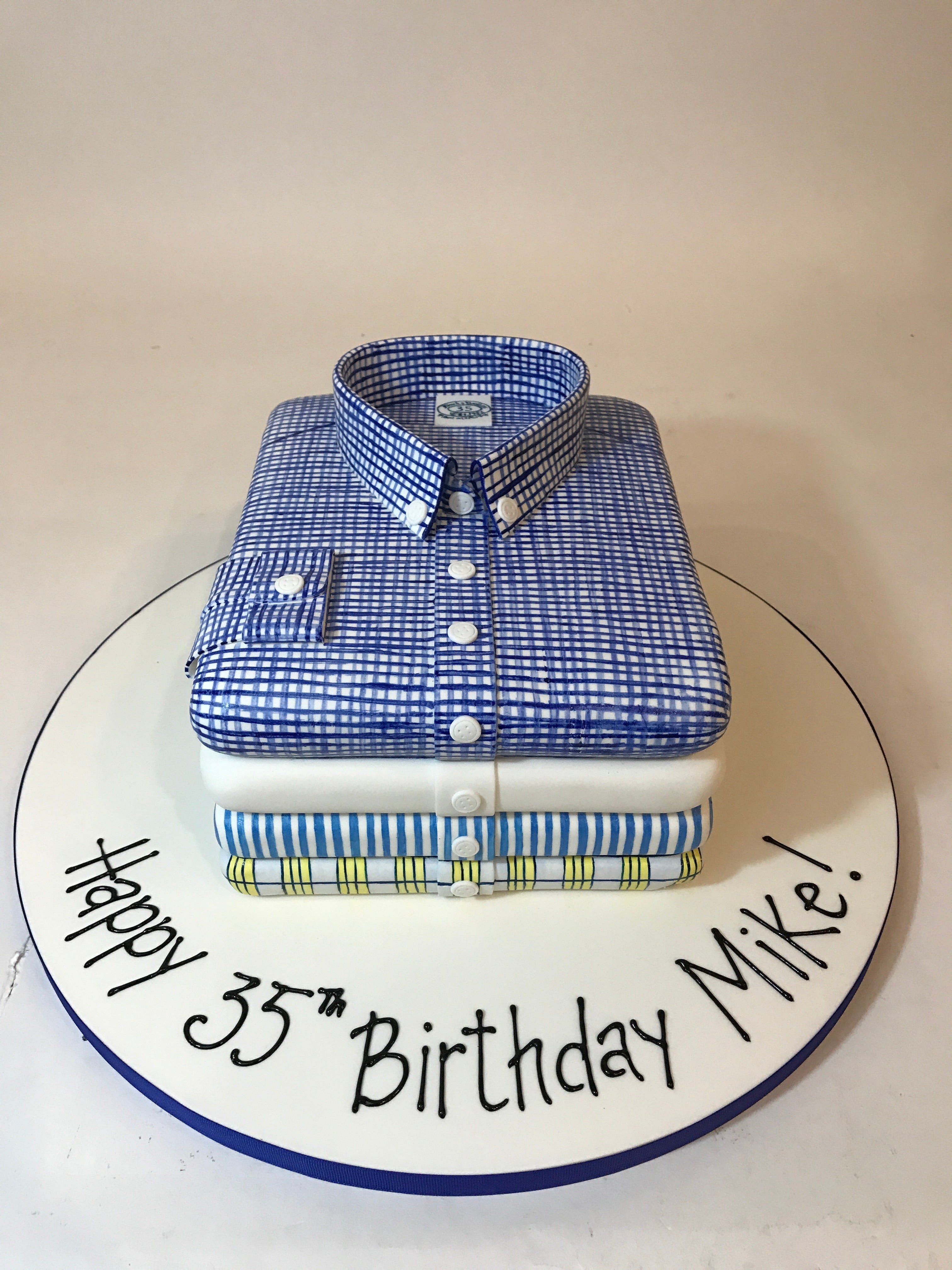 Cake shaped like a blue checkered shirt with 'Happy 35th Birthday Mike!' text on a white background