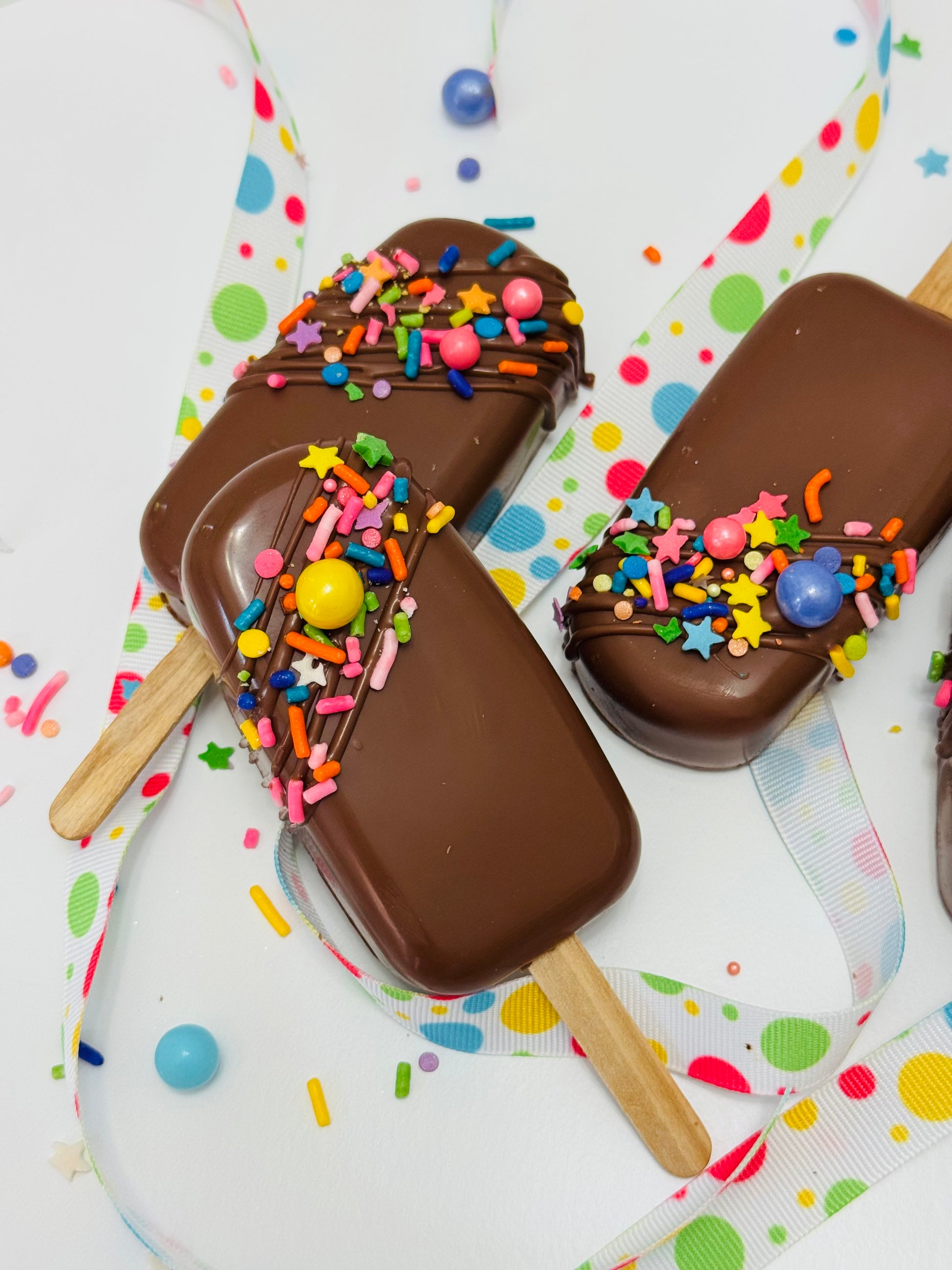 Chocolate-dipped cakesicles with colorful sprinkles on a polka dot background
