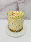 Small round cake with white frosting and colorful sprinkles on a marble background