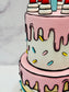 Close-up of a pink cake with white frosting, red candles, and colorful sprinkles on a light gray background.
