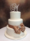 Three-tiered wedding cake with a decorative bow and 'M' monogram on a blurred background