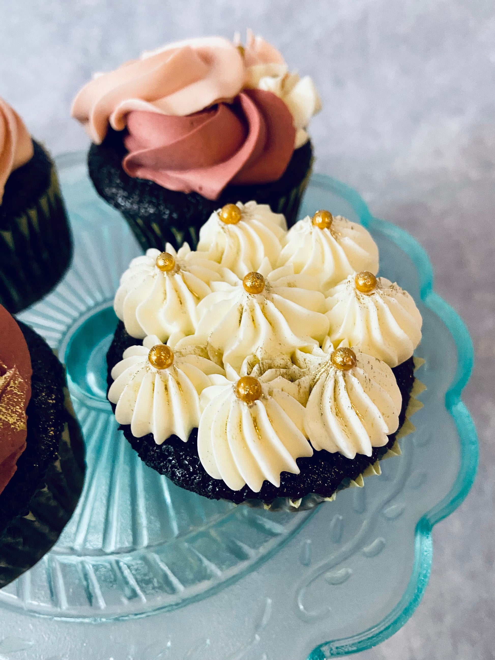 Decorative cupcakes with cream and gold accents on a glass plate.