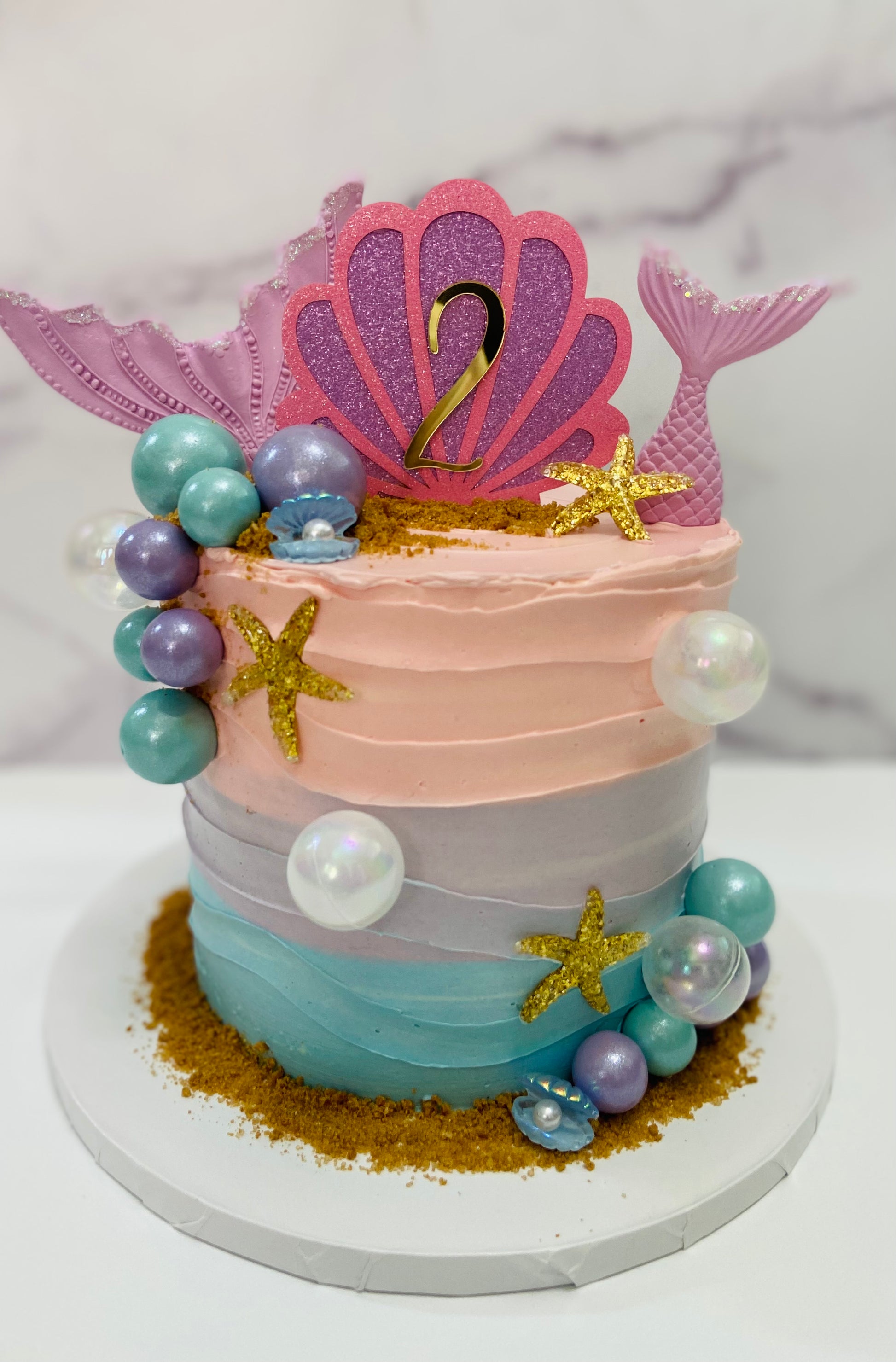 Decorative cake with mermaid-themed decorations on a white marble surface