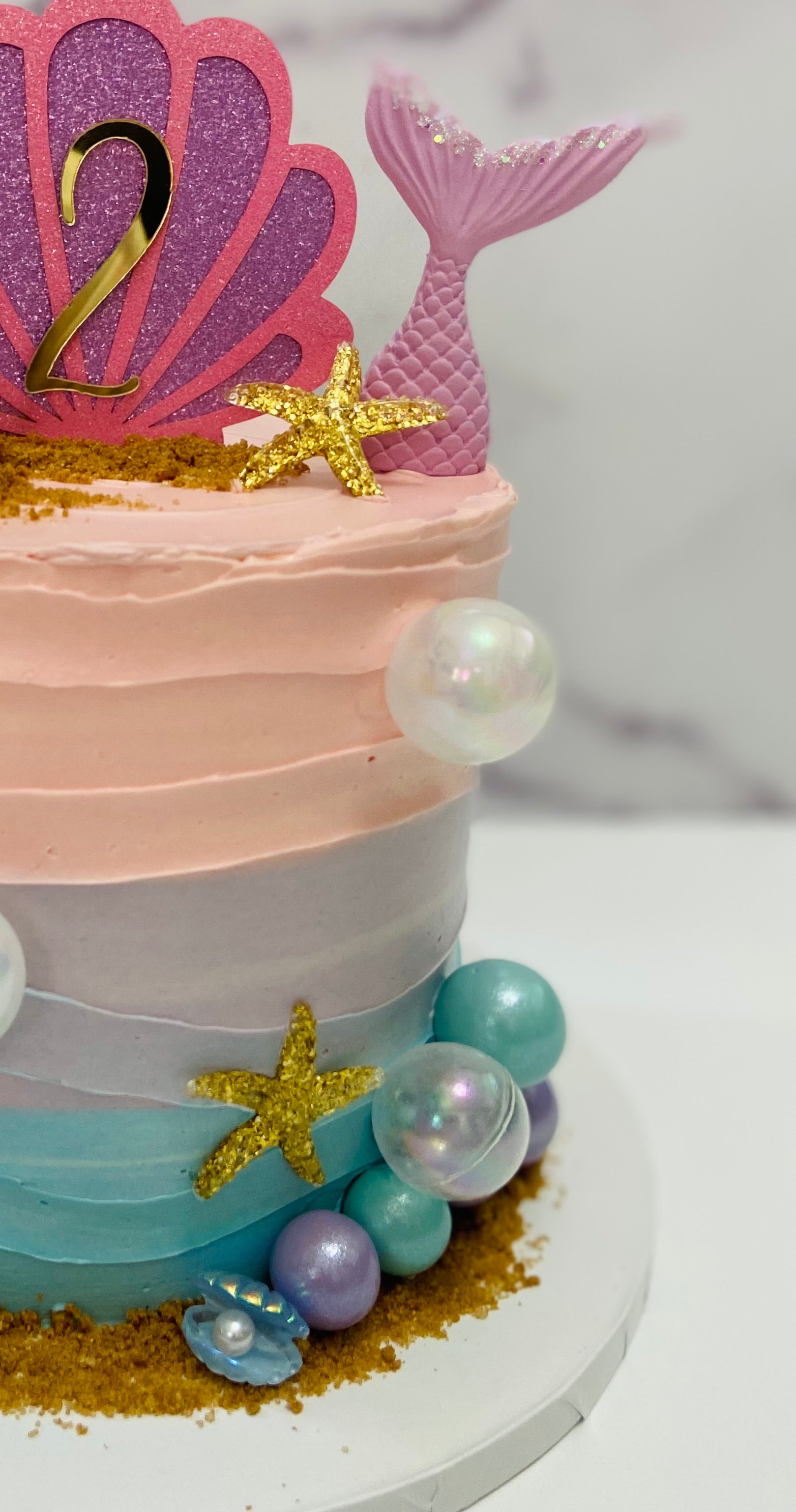 Mermaid-themed birthday cake with pink, blue, and gold decorations on a white background