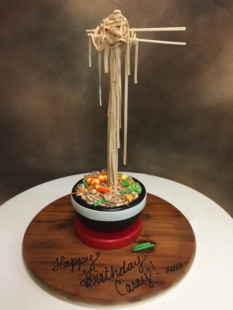 Noodle cake with a wooden base and 'Happy Birthday Casey!' inscription on a brown background