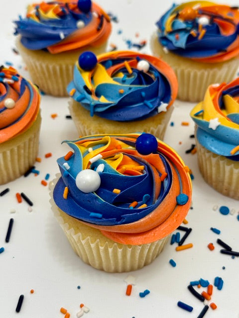 Cupcakes with blue and orange frosting on a white surface with sprinkles.