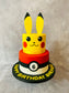 Two-tiered birthday cake designed like Pikachu with a Poké Ball, on a neutral background.