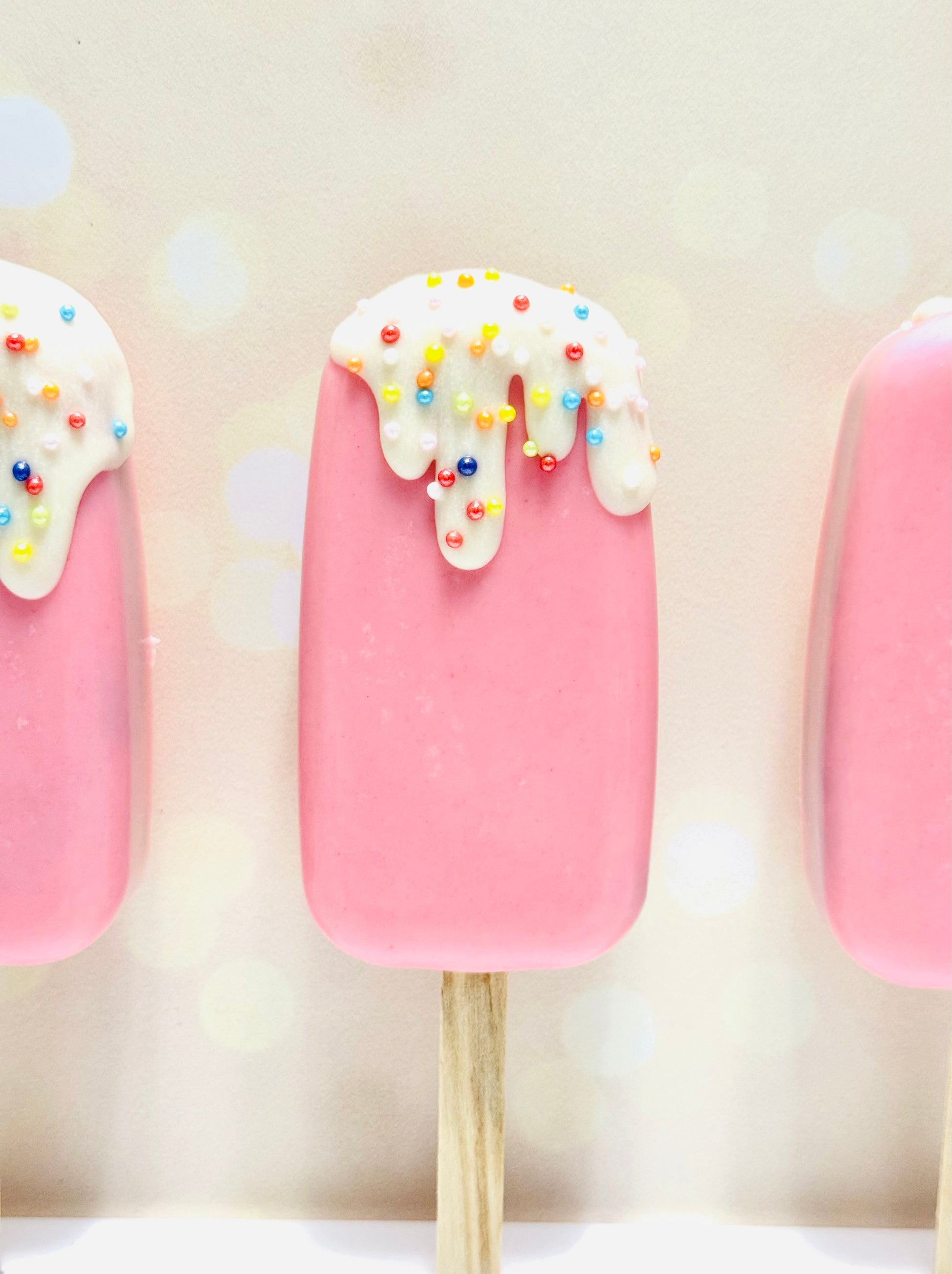 Pink cake pops with white frosting and colorful sprinkles on a light background
