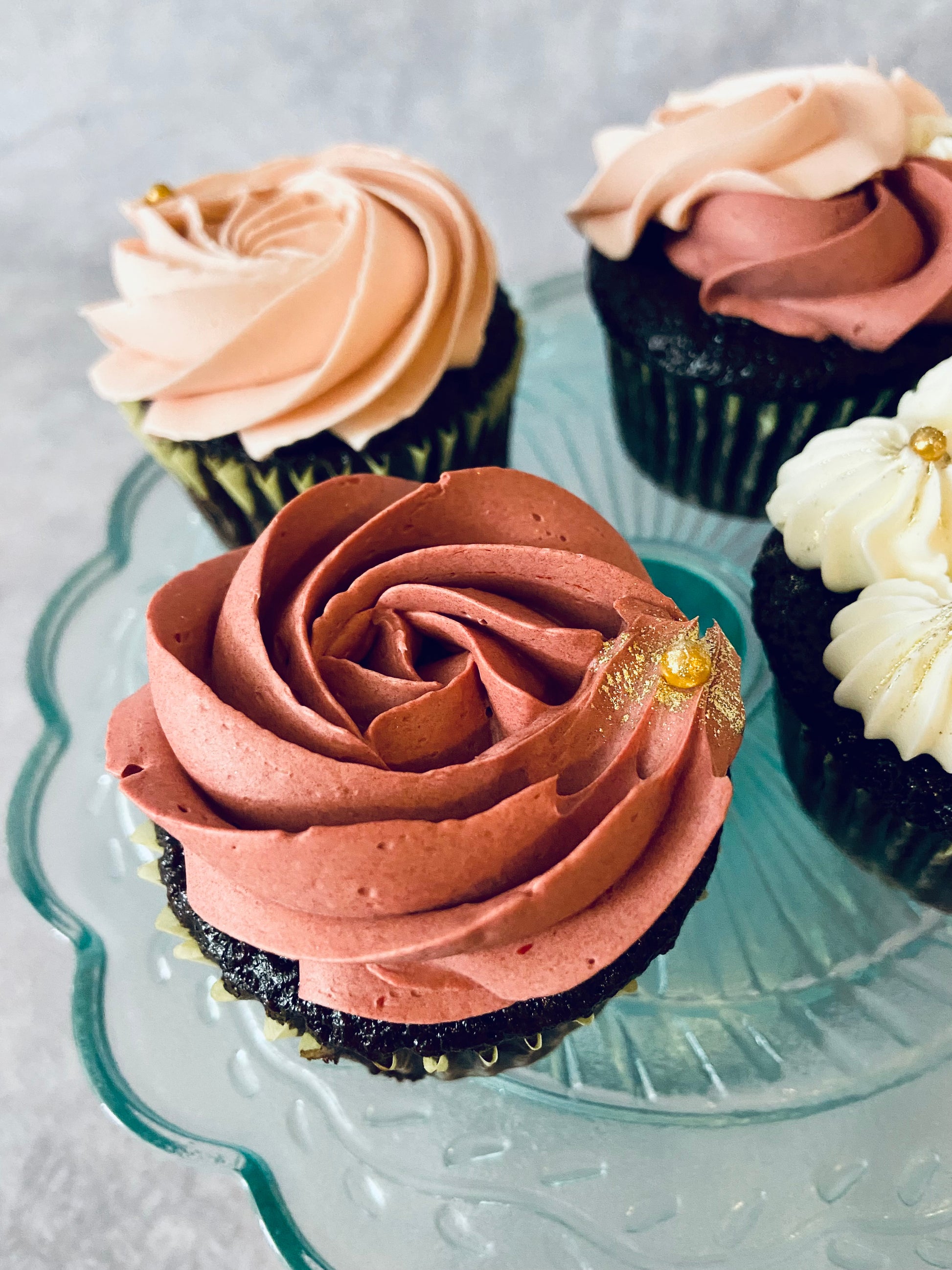 Decorative cupcakes with pink and chocolate frosting on a glass plate.