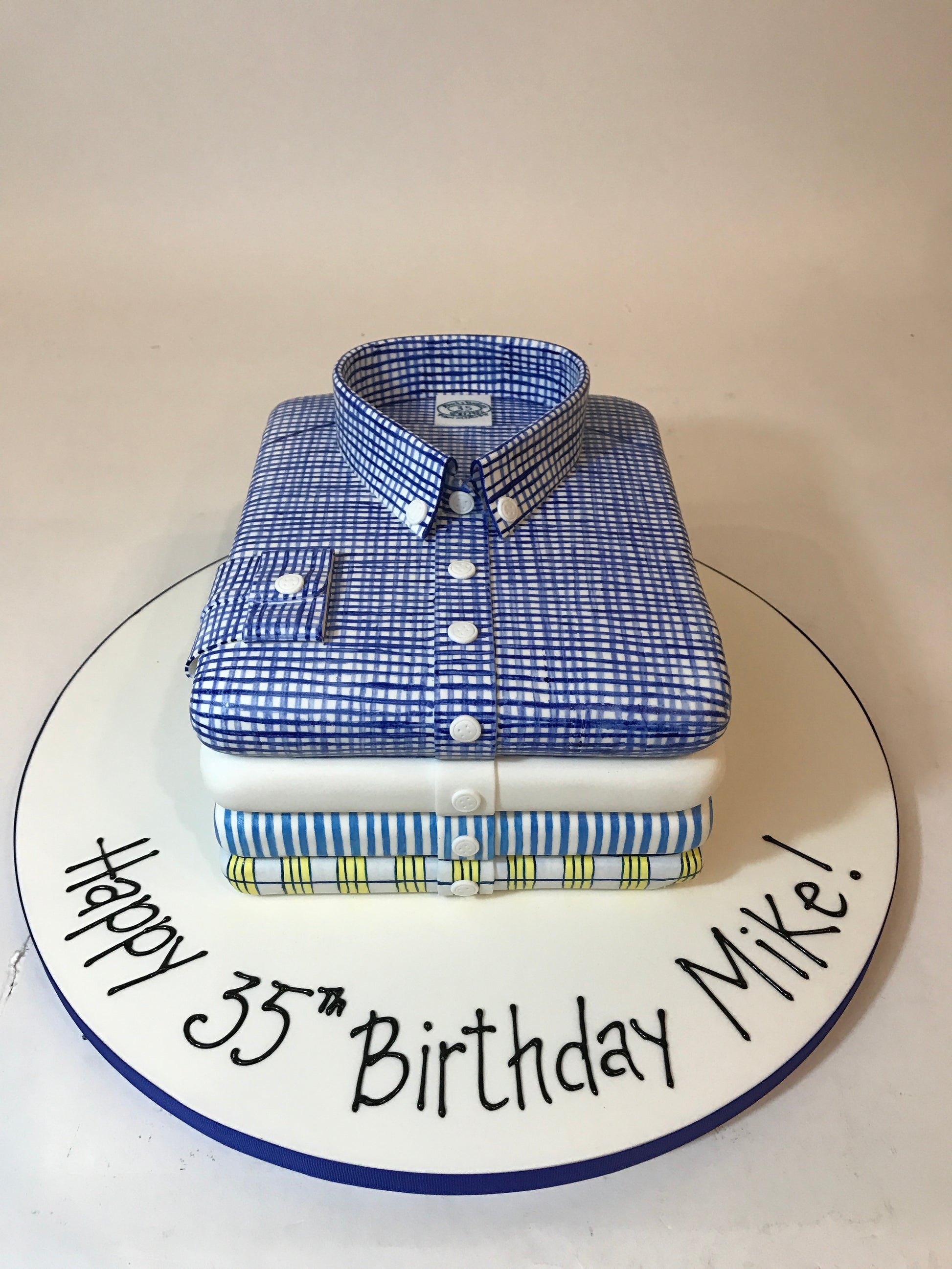 Cake shaped like a blue checkered shirt with 'Happy 35th Birthday Mike!' text on a white background