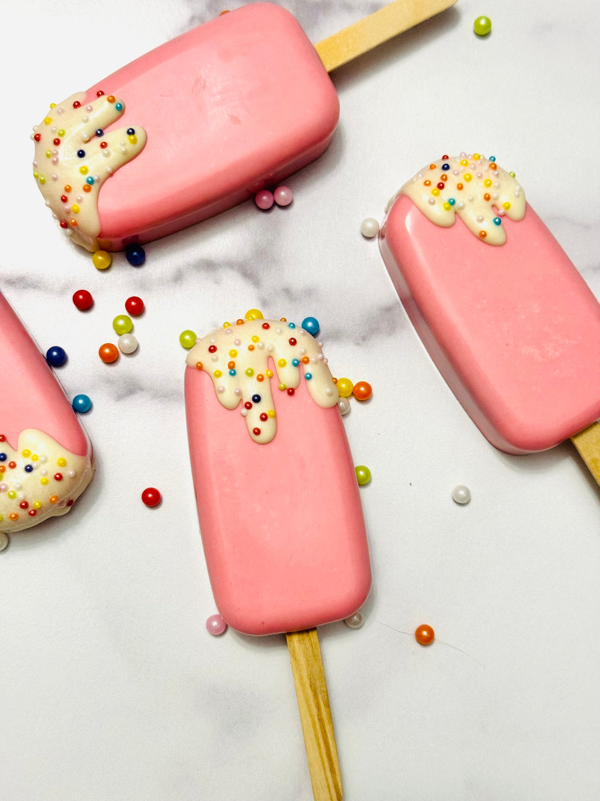 Pink popsicles with white cream and colorful sprinkles on a marble surface