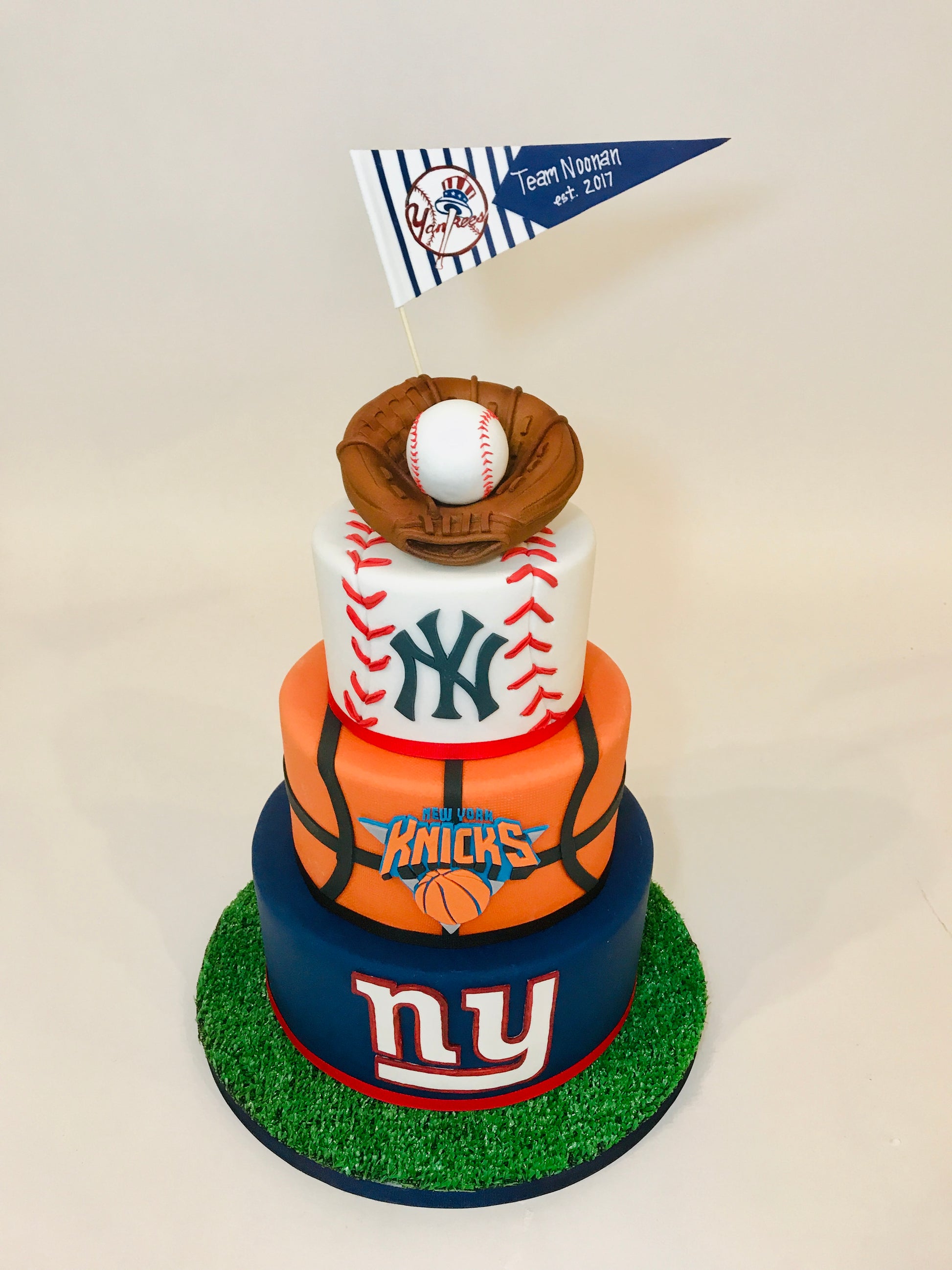 Three-tiered sports-themed birthday cake with baseball, basketball, and football designs on a white background.