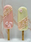 Two decorative popsicle-shaped cakes on sticks with pink and green colors and decorative elements.