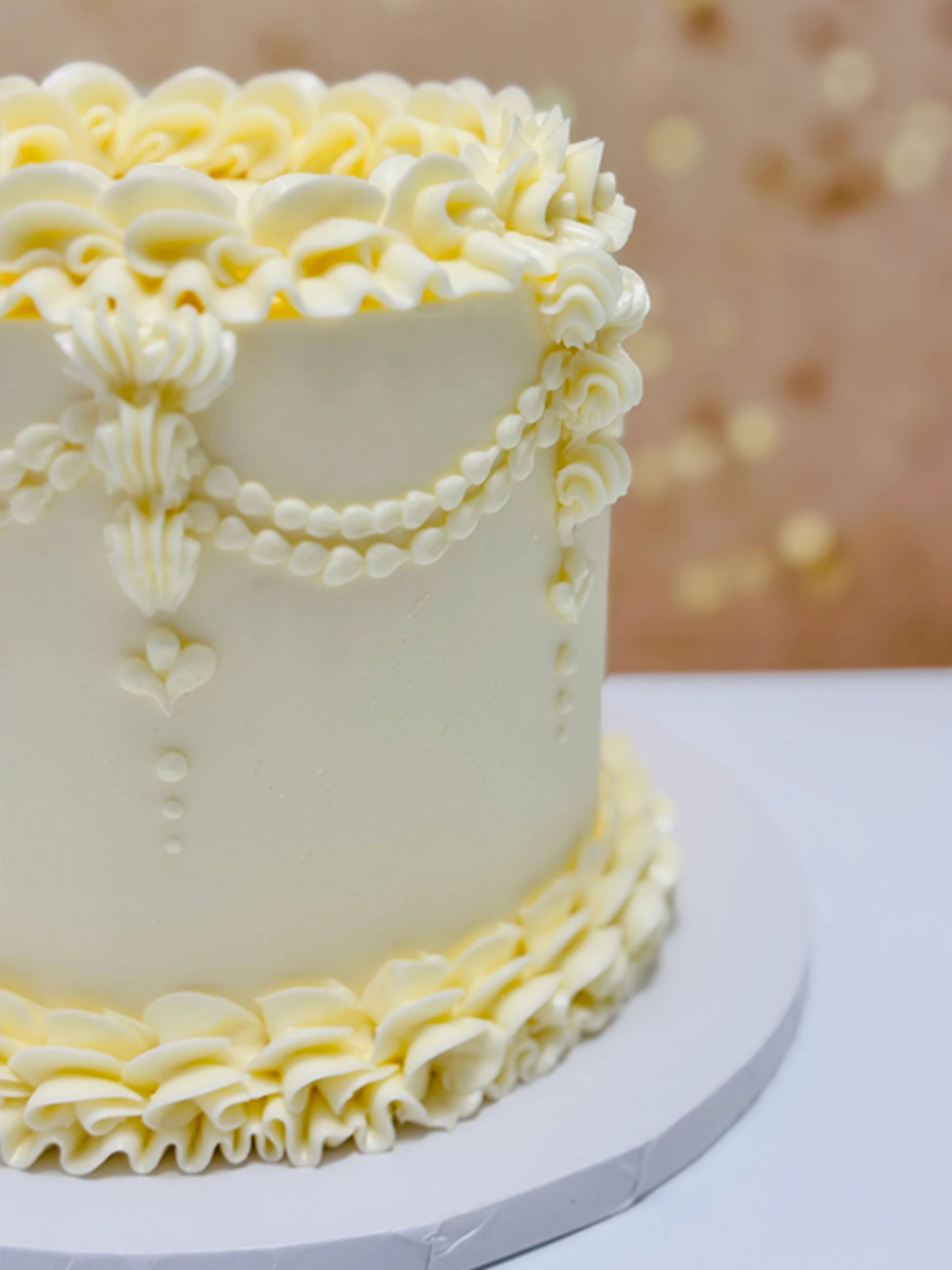 White cake with yellow ruffles on a white surface with a blurred gold background