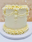 White cake with decorative yellow icing on a white stand against a blurred background