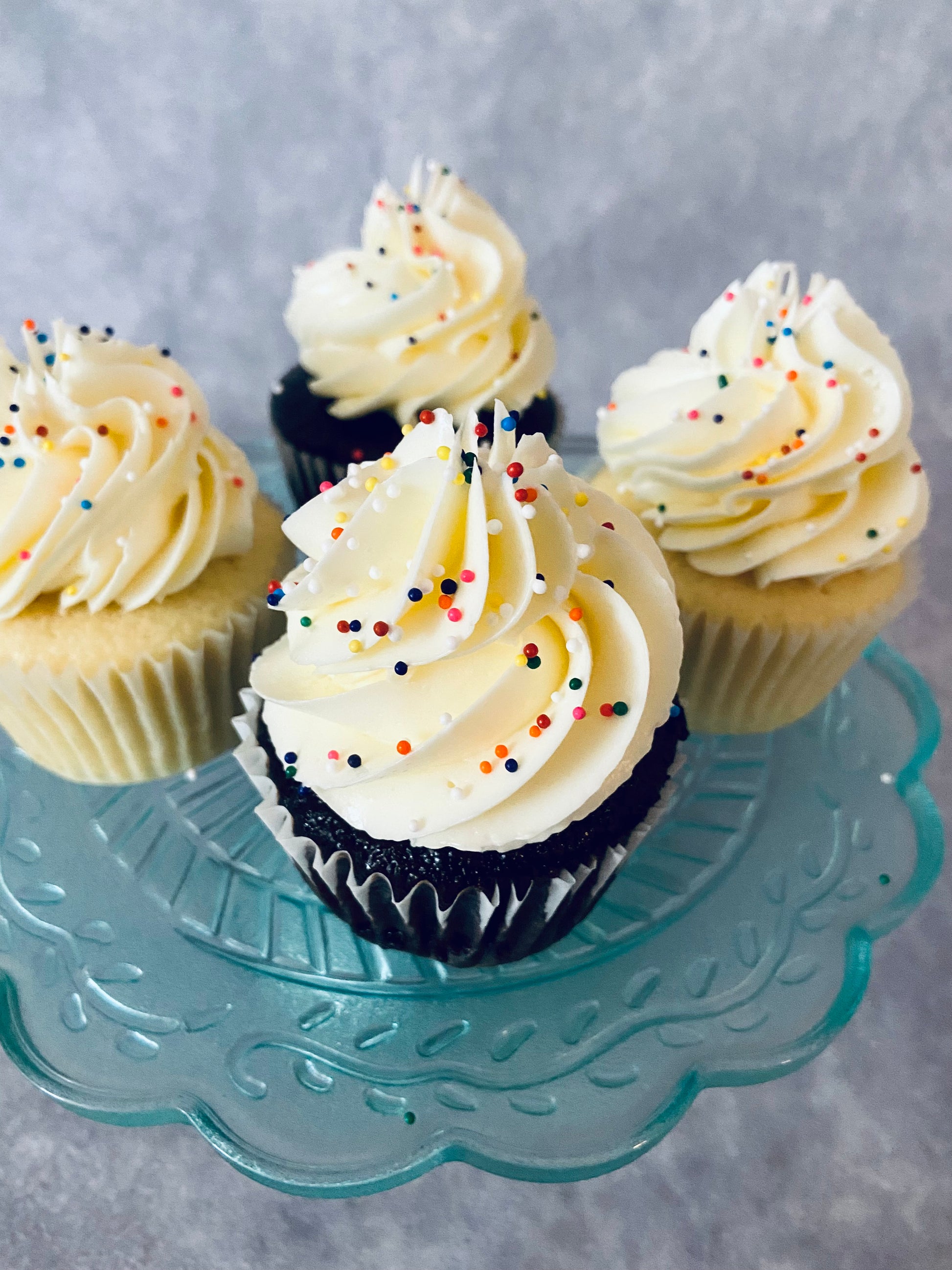 Cupcakes with white frosting and colorful sprinkles on a decorative glass plate.